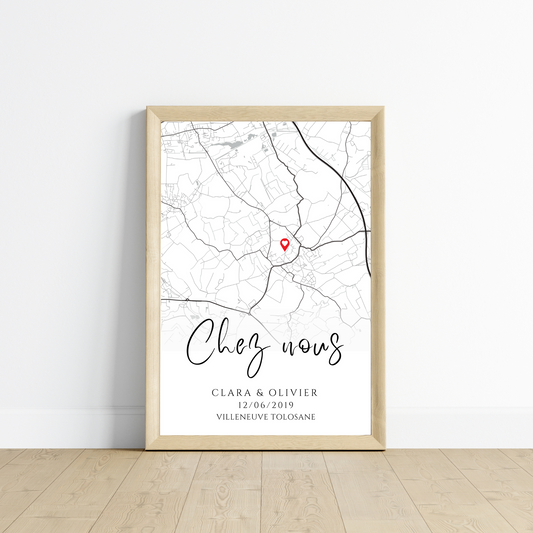 Affiche encadrée avec une carte en noir et blanc marquée d'une épingle rouge. Le texte 'Chez nous' est écrit en calligraphie, suivi des noms 'Clara & Olivier', de la date '12/06/2019' et du lieu 'Villeneuve