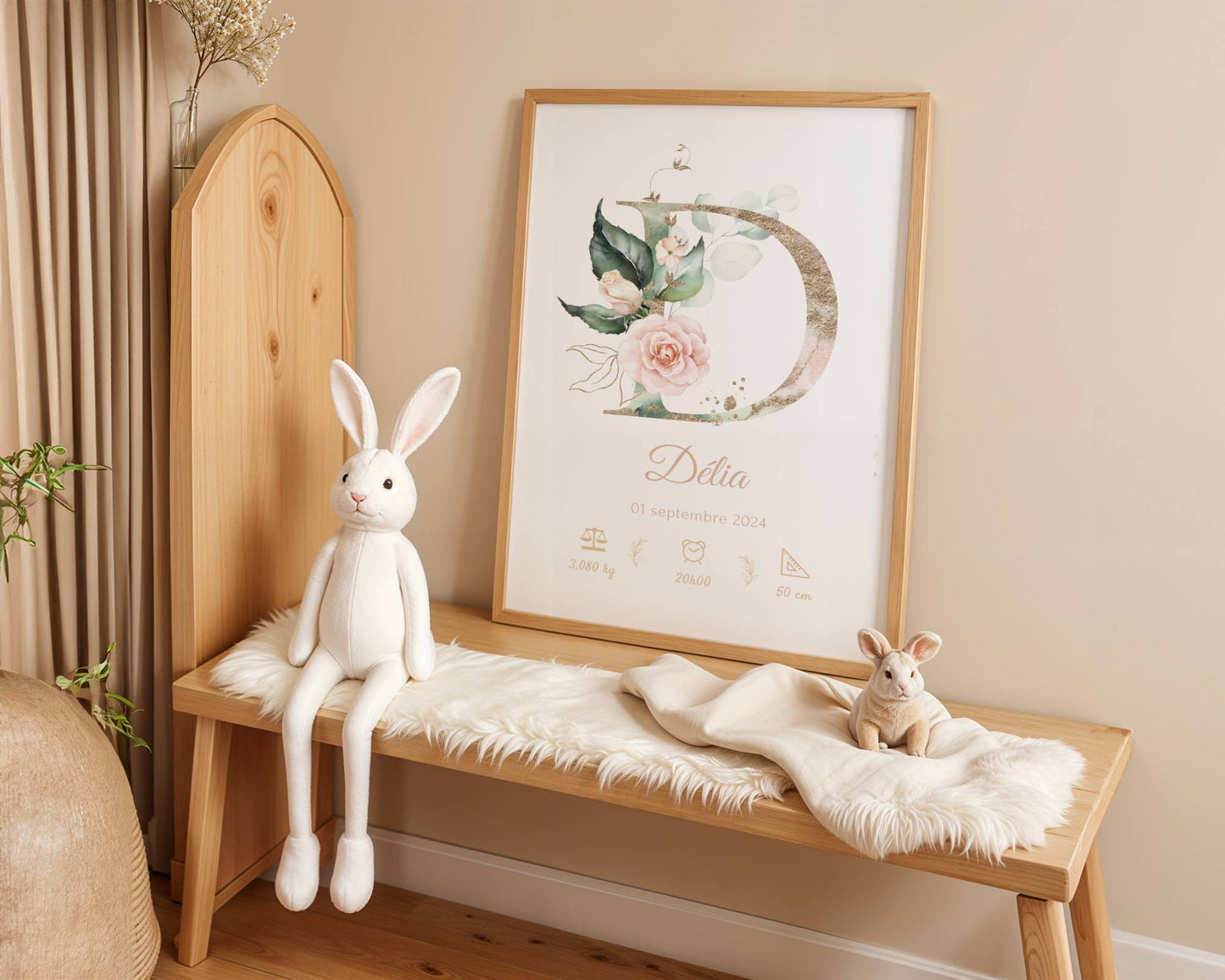 A cozy nursery features a wooden bench, white plush bunny toys, a soft fur throw, and the "Affiche de naissance personnalisée prénom et initiale fleurs rose pastel"—a perfect décor piece and charming cadeau naissance for a little girl's room.