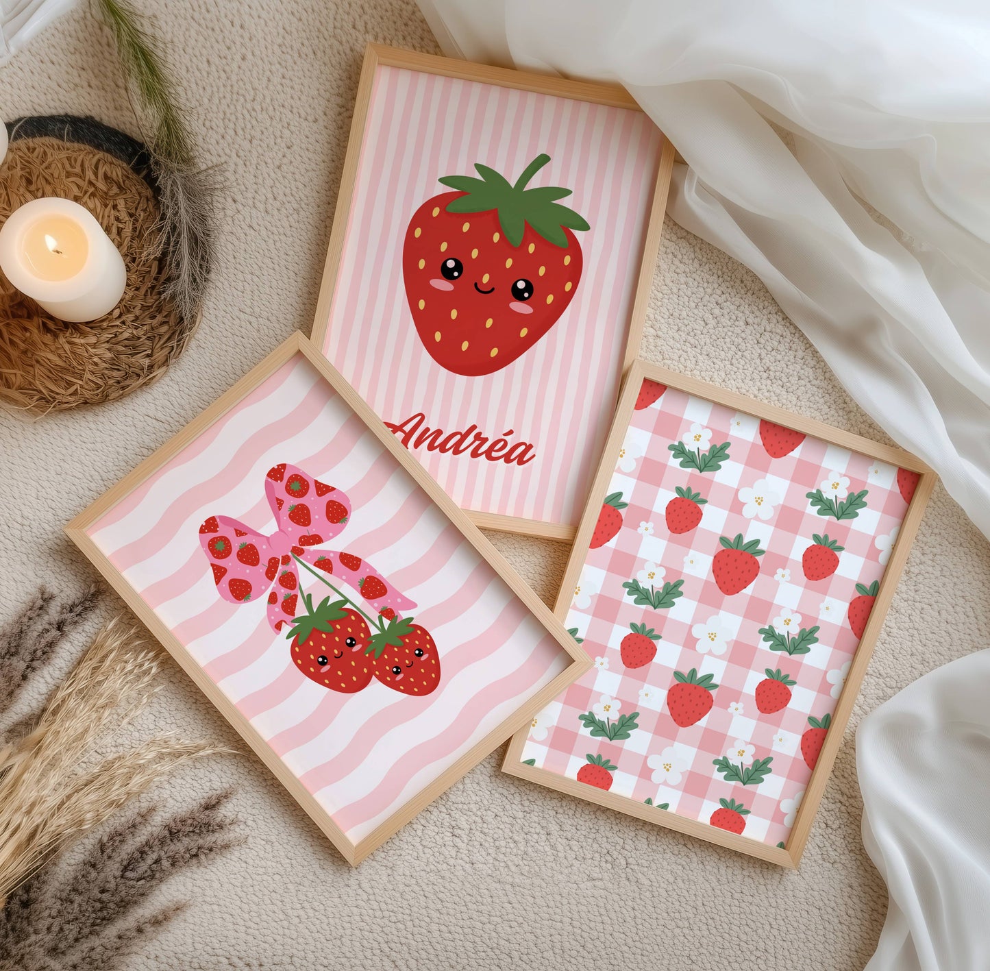 Trio d'affiches murales enfantines au thème fraise kawaii et esthétique coquette. La première affiche présente un motif vichy rose et blanc parsemé de fraises et fleurs blanches. La seconde, centrale, montre une grande fraise souriante personnalisée avec le prénom Andréa sur fond rayé rose. La troisième affiche illustre deux fraises kawaii suspendues à un ruban rose à motifs fraises sur un fond de vagues roses. Palette de couleurs rouge, rose pastel et vert.