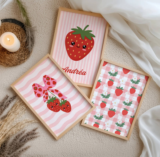 Trio d'affiches murales enfantines au thème fraise kawaii et esthétique coquette. La première affiche présente un motif vichy rose et blanc parsemé de fraises et fleurs blanches. La seconde, centrale, montre une grande fraise souriante personnalisée avec le prénom Andréa sur fond rayé rose. La troisième affiche illustre deux fraises kawaii suspendues à un ruban rose à motifs fraises sur un fond de vagues roses. Palette de couleurs rouge, rose pastel et vert.