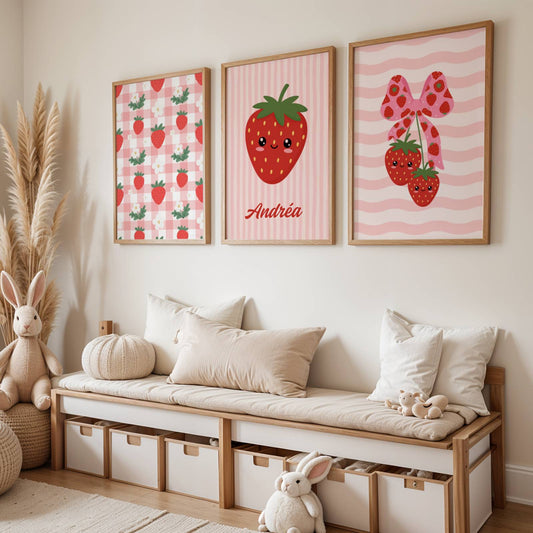 Trio d'affiches murales enfantines au thème fraise kawaii et esthétique coquette. La première affiche présente un motif vichy rose et blanc parsemé de fraises et fleurs blanches. La seconde, centrale, montre une grande fraise souriante personnalisée avec le prénom Andréa sur fond rayé rose. La troisième affiche illustre deux fraises kawaii suspendues à un ruban rose à motifs fraises sur un fond de vagues roses. Palette de couleurs rouge, rose pastel et vert.